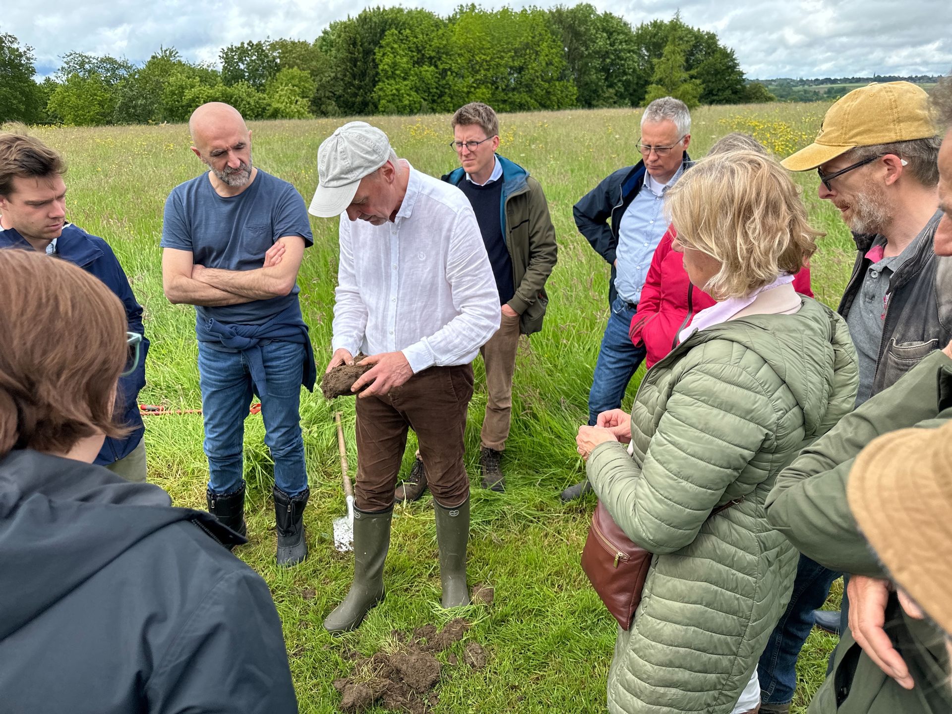 Groupe d'adultes dans un champs vert entourant le formateur en agroécologie tenant un morceau de terre compacte en main